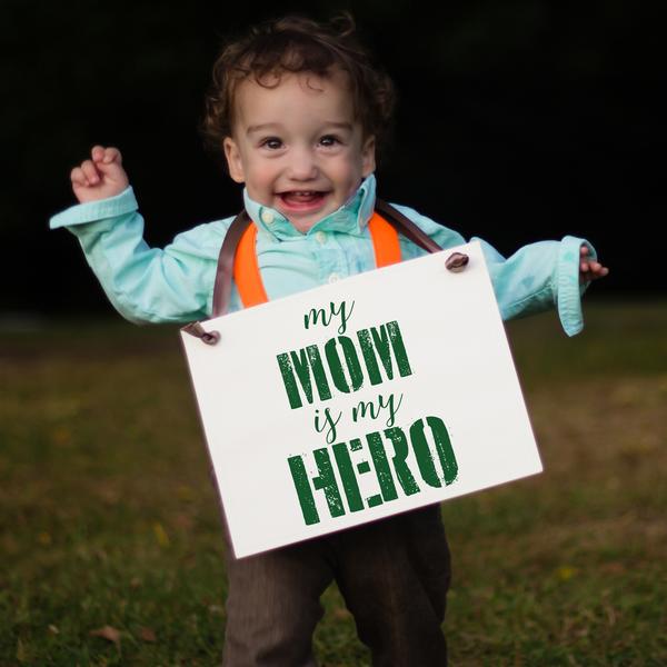 a toddler with a sign that reads my mom is my hero