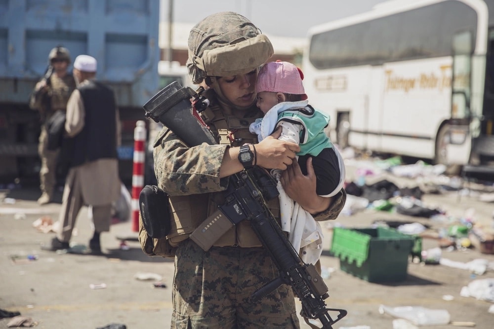 A U.S. Marine with the 24th Marine Expeditionary Unit (MEU) carries a baby as the familiy processes through the Evacuation Control Center (ECC) during the evacuation at Hamid Karzai International Airport, 8/28/21 (U.S. Marine Corps photo)