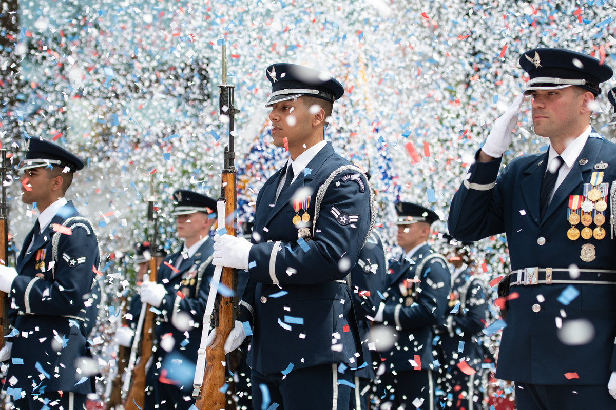 Several air men standing in formation holding rifles and confetti is falling