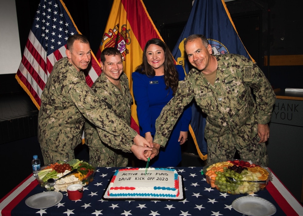 navy sailors pose over a cake cutting