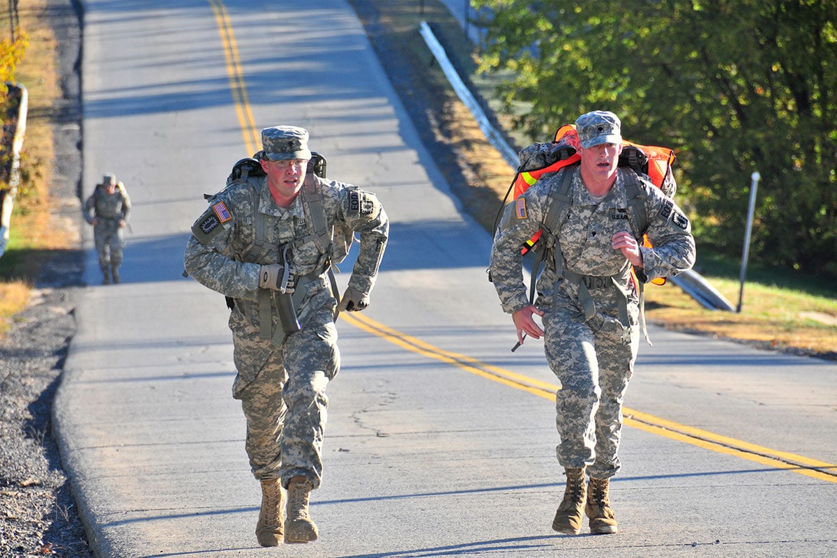 two army soldiers run up an incline with rucks